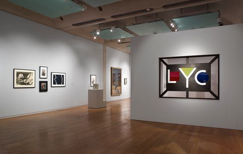 Installation. Five works of art on two walls in the space we occupy are spotlighted in a dimmed gallery. A sign across from us shows geometric shapes tucked into initials: a red square in a capital L, a yellow triangle filling the top of a Y, and a blue circle hugged by a C.